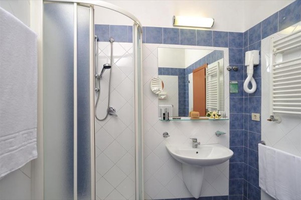 Moderní koupelna s modro-bílými kachličkami, sprchovým koutem, umyvadlem a zrcadlem.