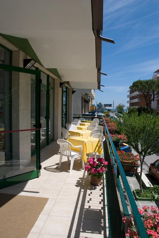 Balkon s bílými plastovými židlemi a žlutými ubrusy, obklopený květinami.