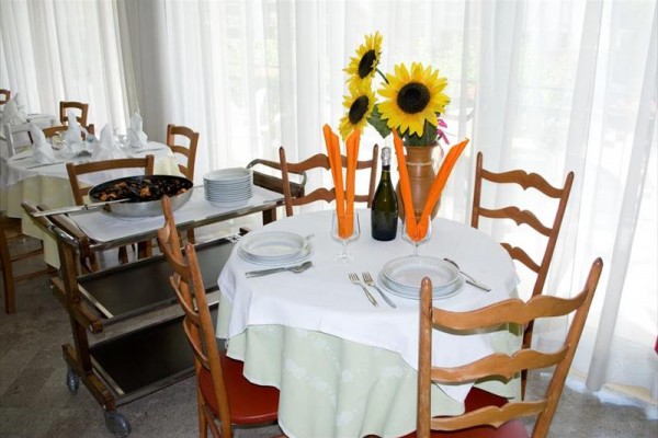 Stůl v restauraci s prostíráním, lahví a váza se slunečnicemi.