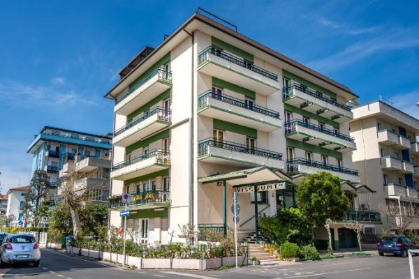 Čtyřpatrová budova s balkónem na rohu ulice za slunečného dne.