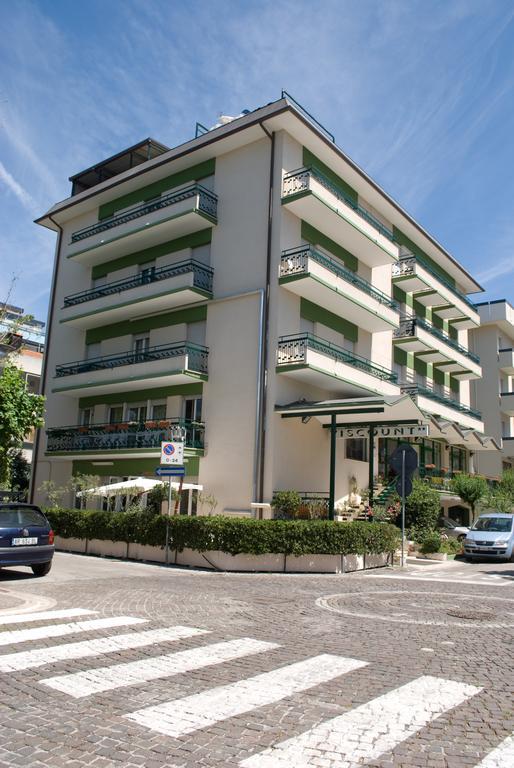 Čtyřpatrová budova s balkony a parkovištěm před ní.