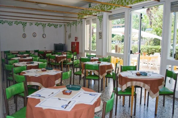 Restaurace s kruhovými stoly, zelenými židlemi a venkovním posezením.