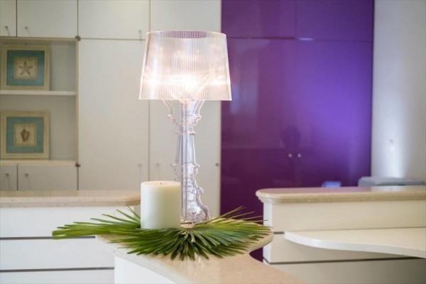 Stolní lampa s bílým svíčkou a zelenými listy na moderní recepci s fialovou stěnou.