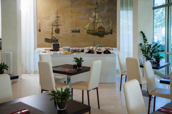 Restaurace s bílými židlemi, stolem s občerstvením a velkou malbou lodí na zdi.