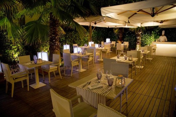 Venkovní restaurace s dřevěnými stoly a židlemi pod bílými slunečníky.