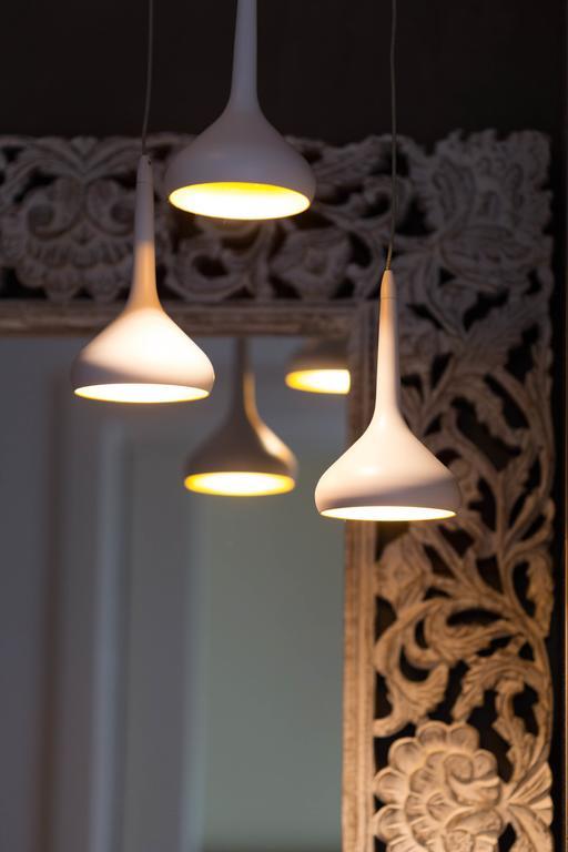 Bílé závěsné lampy před zrcadlem s ozdobným rámem.