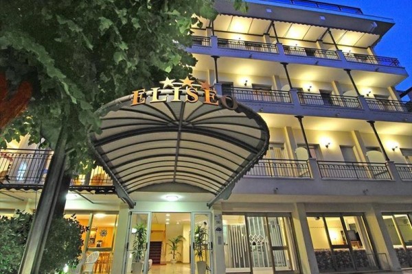 Pětipatrová budova hotelu se světelným nápisem a markýzou při vstupu, viděná zespodu za soumraku.  