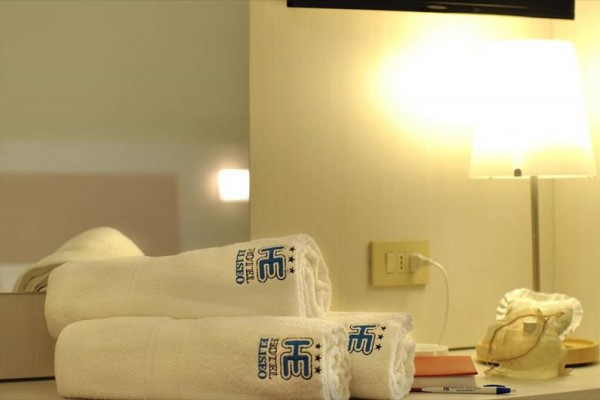 Bílé ručníky s logem hotelu u lampy na stolku.