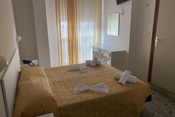 Ložnice s manželskou postelí, zlatým povlečením a televizí na stěně.