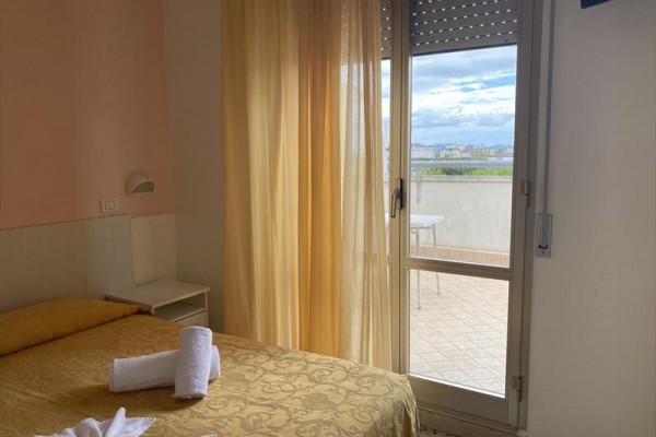 Pokoj s postelí, ručníky a otevřenými dveřmi na balkon.