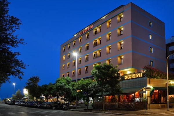 Noční pohled na osvětlenou budovu hotelu Rossini obklopenou stromy.