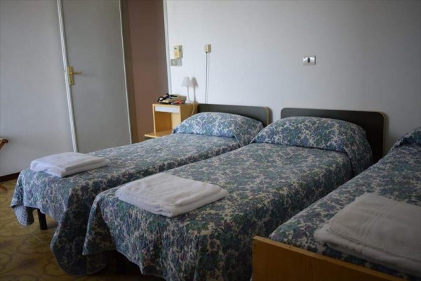 Tři jednolůžkové postele s květinovým přehozem a ručníky v řadě.