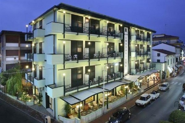 Třípatrový hotel s večerním osvětlením a balkony.