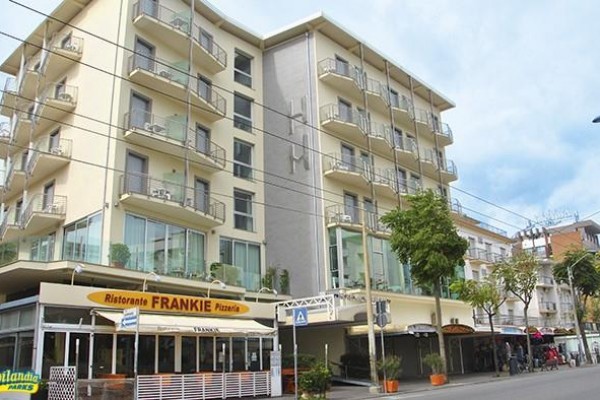 Moderní šestiúrovňová budova na rohu ulice s restaurací Pizzeria Frankie v přízemí.