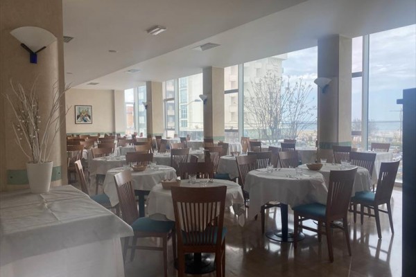 Restaurace s kruhovými stoly a dřevěnými židlemi u velkých oken s výhledem.