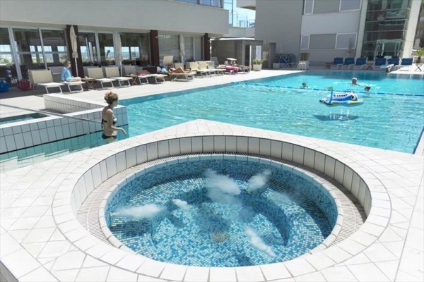 Vířivka a bazén u moderního hotelu se slunečními lehátky.