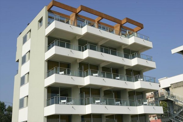 Moderní šestipatrová budova s balkony a pergolou na střeše.