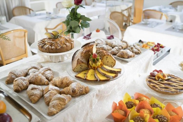 Různé druhy pečiva a dortů na elegantně prostřeném stole v restauraci.