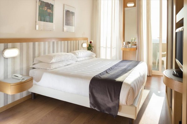 Moderně zařízená hotelová ložnice s manželskou postelí a balkonem.  