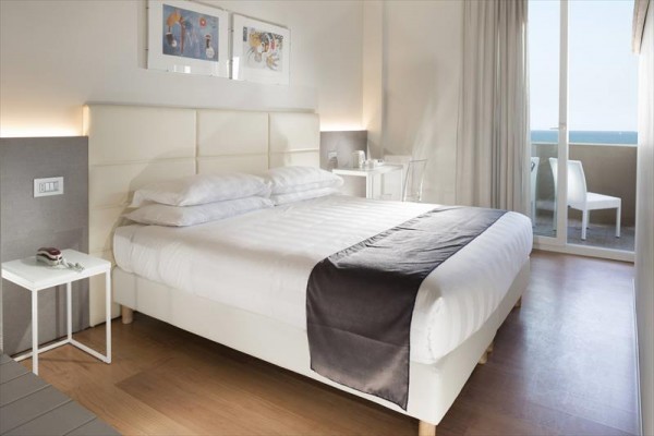 Moderní hotelový pokoj s velkou postelí a balkonem s výhledem na moře.  