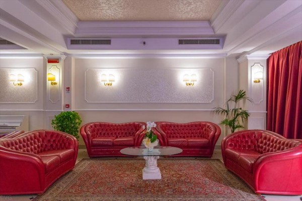 Červené kožené sedací soupravy a skleněný stolek v elegantní místnosti s koberci a rostlinami.
