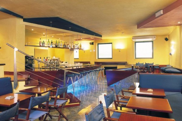 Moderní bar s vysokými židlemi, dřevěnými stoly a skleničkami na pultu.