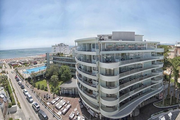 Moderní hotel u moře s balkony a velkým bazénem vedle pláže.