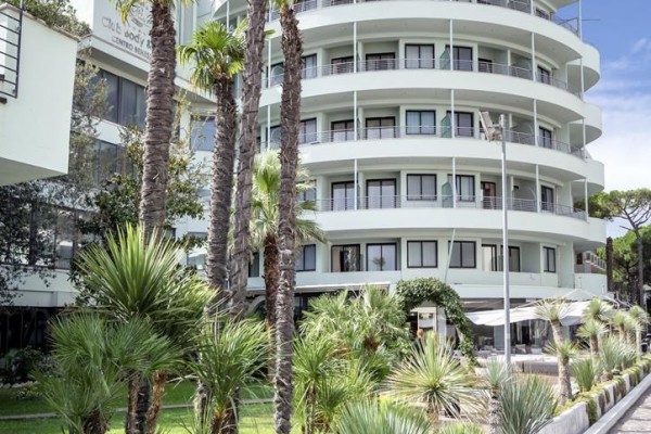 Moderní zaoblená budova s balkony obklopená palmami a zelení.