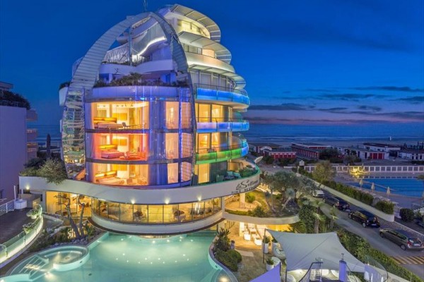 Moderní hotel se barevným večerním osvětlením a bazénem v popředí.