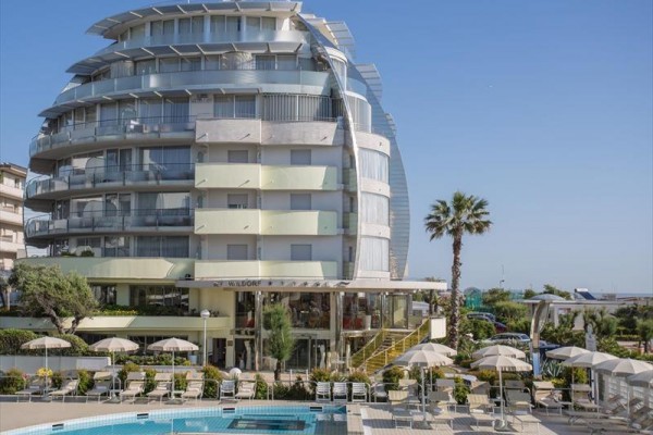 Moderní hotel s bazénem a venkovními lehátky pod slunečníky.