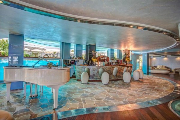 Elegantní bar s bílým klavírem a zakřiveným pultem uprostřed světlého prostoru.