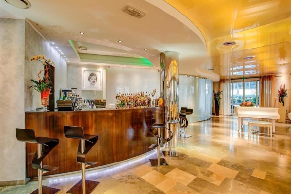 Stylový moderní bar s dřevěným pultem, vysokými židlemi a bílým piánem v pozadí.