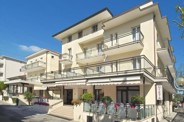 Moderní budova hotelu se třemi patry a balkóny, obklopená rostlinami.