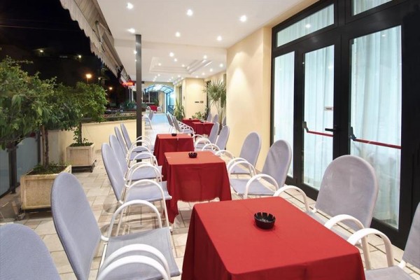 Terasa restaurace s červenými ubrusy na stolech a bílými židlemi.
