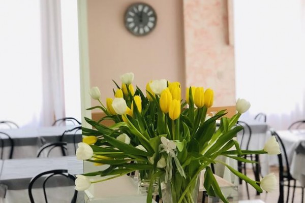 Váza s bílými a žlutými tulipány na stolku v místnosti s hodinami na zdi.