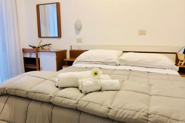 Ustlaná postel s bílými ručníky a květinou na dece v ložnici.