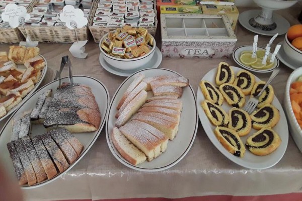 Dezerty a pečivo vystavené na talířích s balenými marmeládami a čajem v pozadí. 