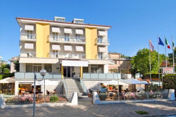 Čtyřpatrový hotel se žlutými balkony a slunečníky před vchodem.