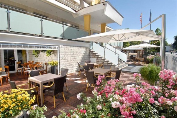 Terasa restaurace s dřevěnými stoly, židlemi a květinami pod slunečníky.