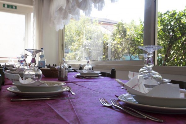 Stůl se nachází v restauraci, prostřený s fialovým ubrusem, talíři a sklenicemi.