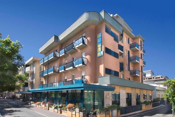 Moderní hotel s balkony a proskleným přízemím na rohu ulice za jasného počasí.
