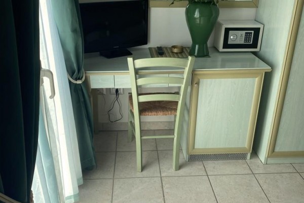 Stůl s židlí, počítačovým monitorem a vázi s květinami u okna.