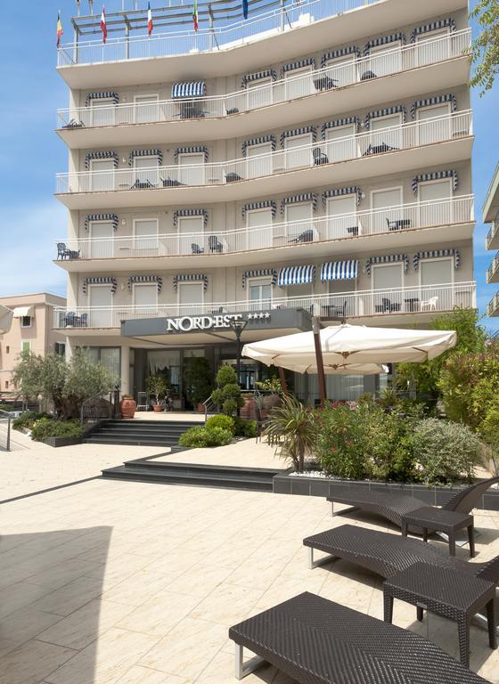 Budova hotelu Nord Est s více balkony a venkovním posezením pod slunečníkem.