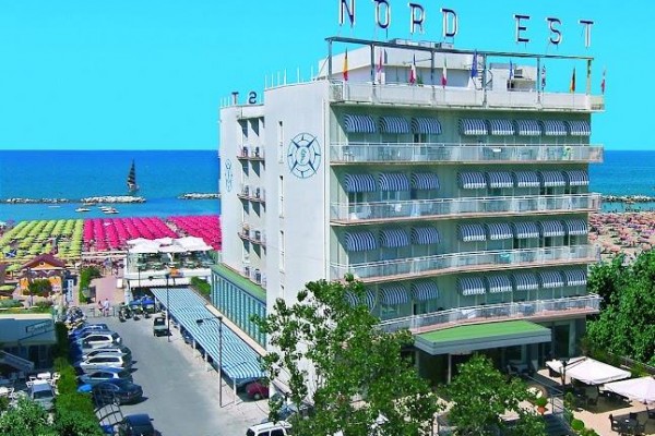 Hotel Nord Est u pláže s barevnými slunečníky a modrou oblohou v pozadí.