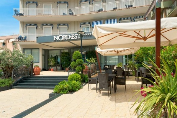 Exteriér hotelu se stolky a slunečníky na terase.