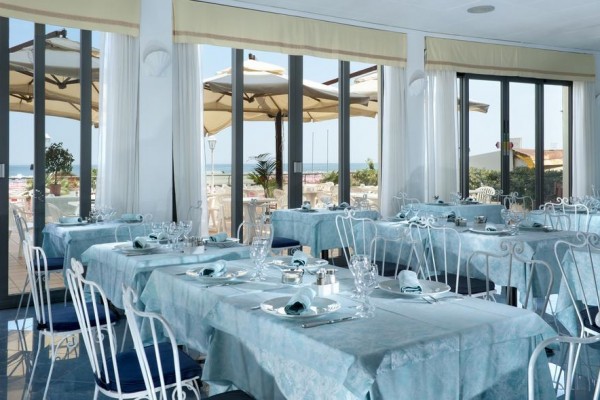 Restaurace s modrými ubrusy a výhledem na terasu se slunečníky.