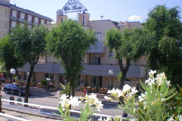 Hotel obklopený zelenými stromy a květinami na předzahrádce.