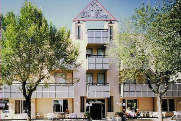 Fasáda hotelu obklopená stromy s venkovními stoly a židlemi.