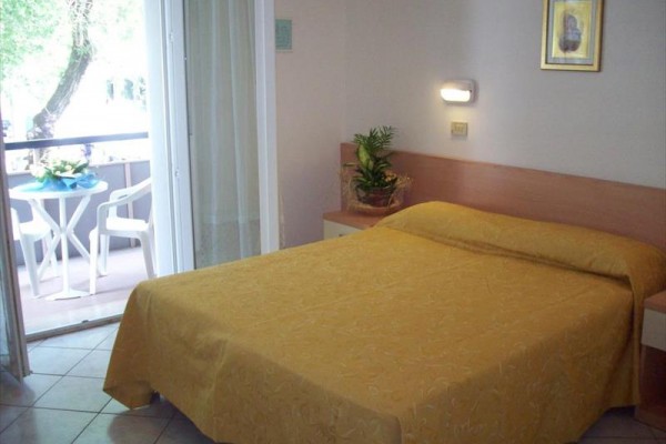 Pokoj s manželskou postelí, nočním stolkem a balkonem s výhledem ven.