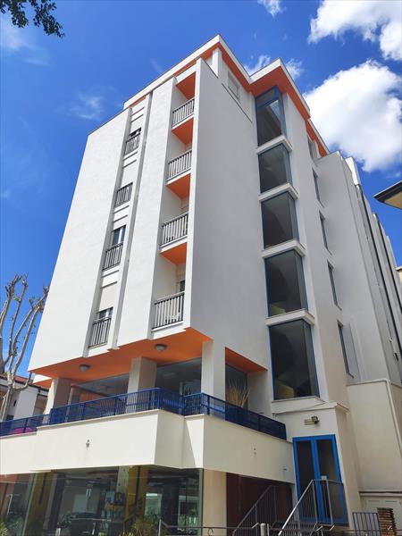 Moderní šestipatrová budova s oranžovými prvky proti modré obloze.